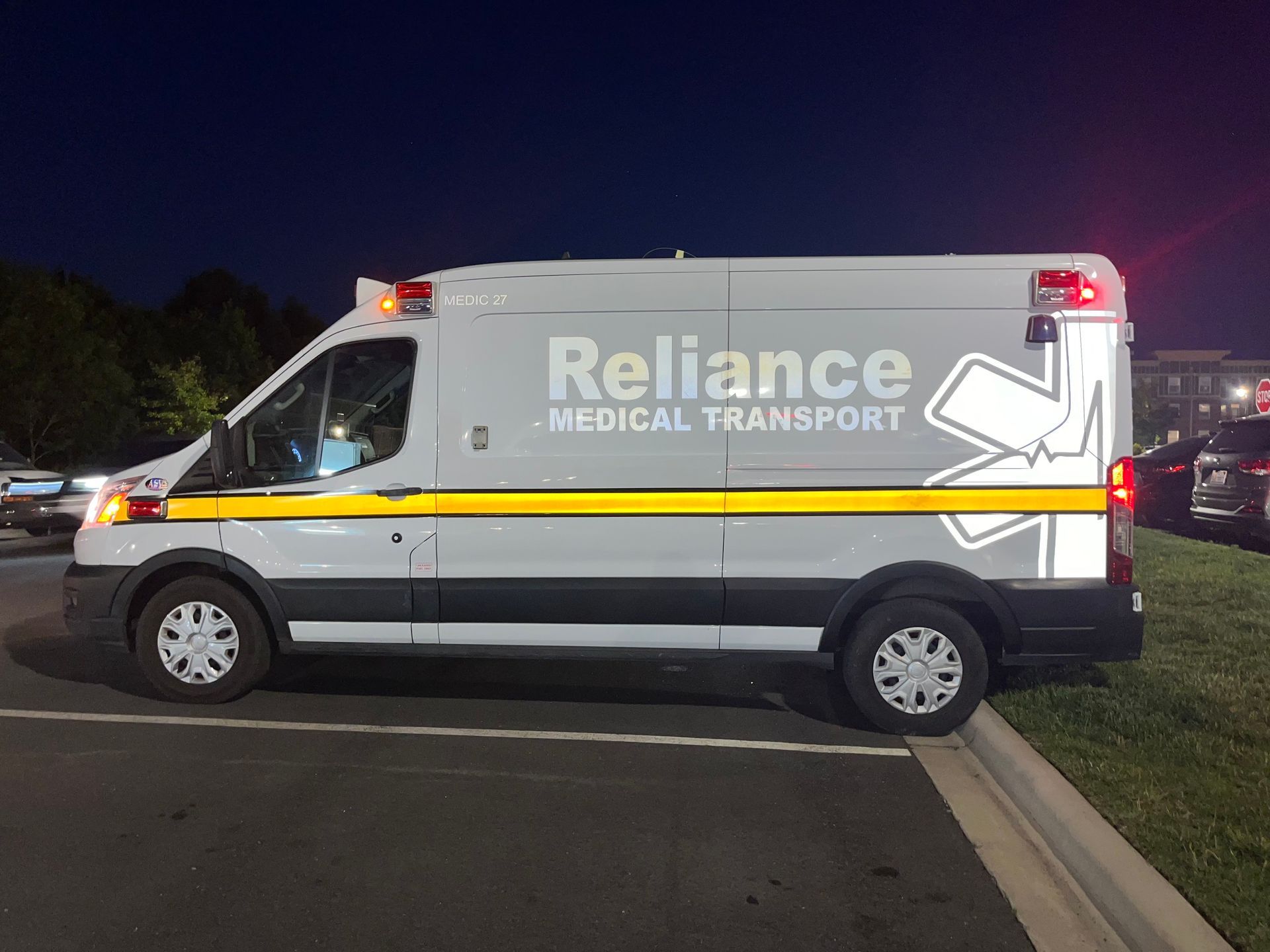 Reliance Medical Transport ambulance parked at night with flashing lights.