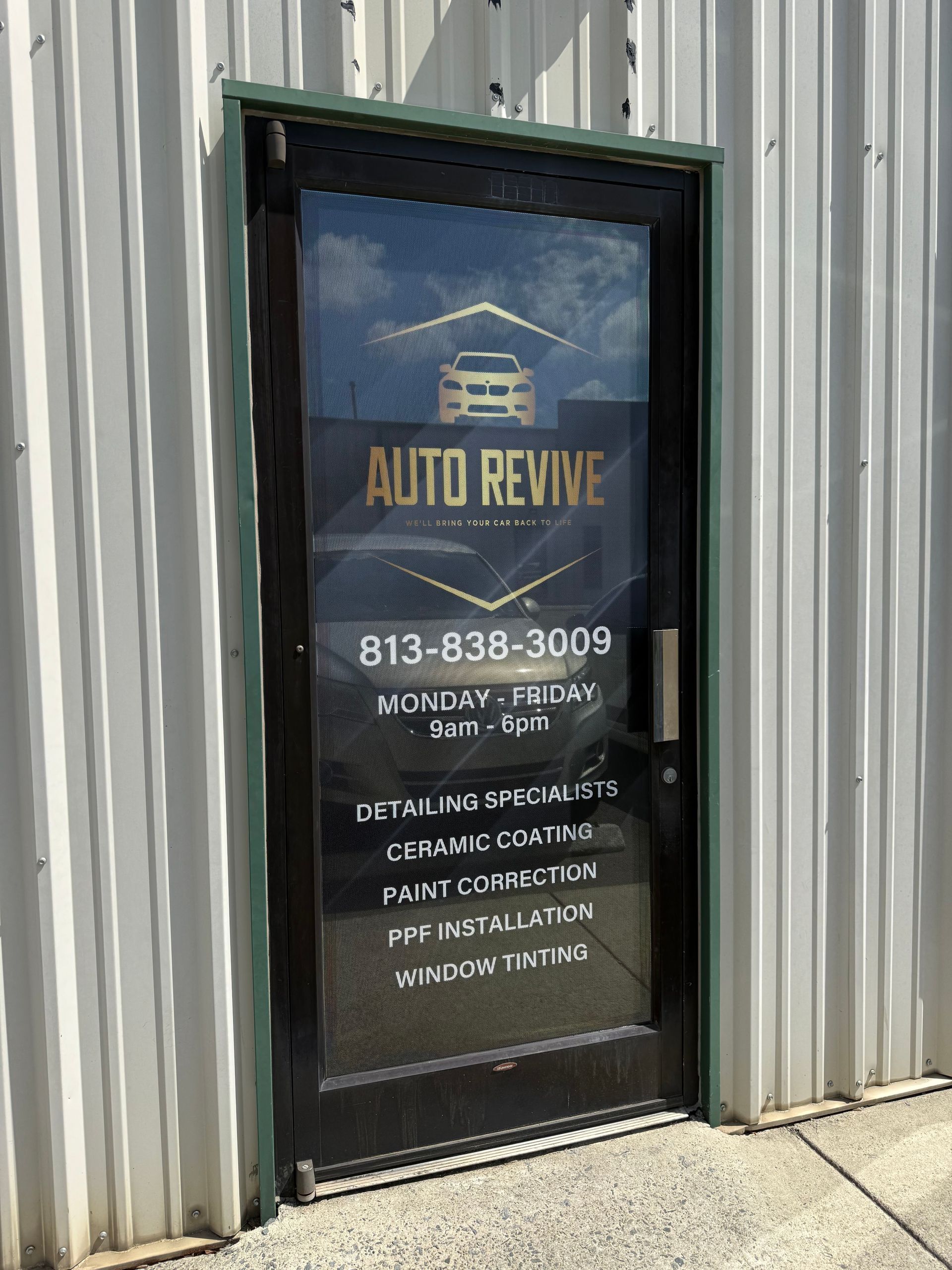 Auto repair shop door with window sign and business hours on a corrugated metal building