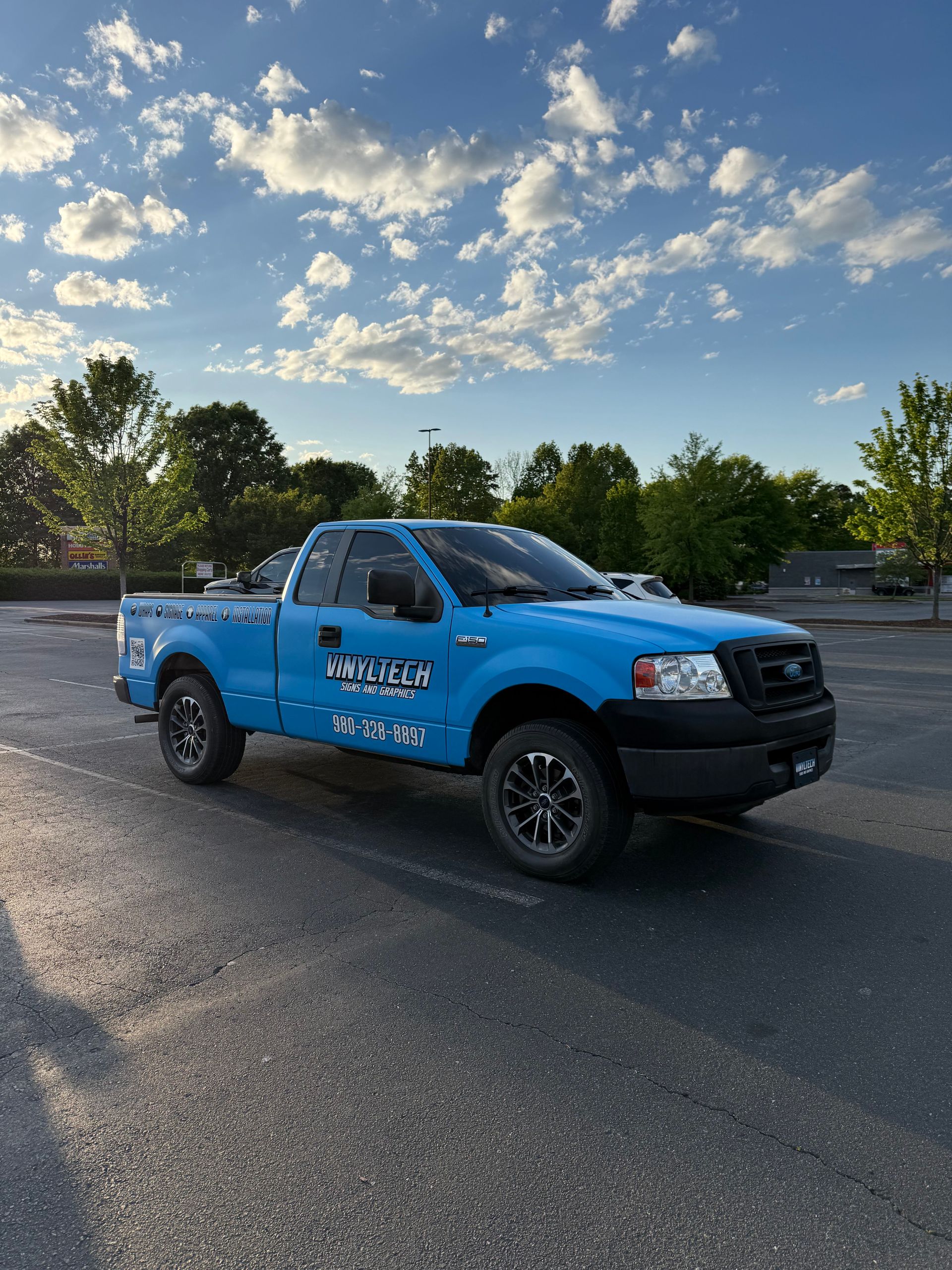 Blue pickup truck parked in a lot at sunset under a sky with scattered clouds