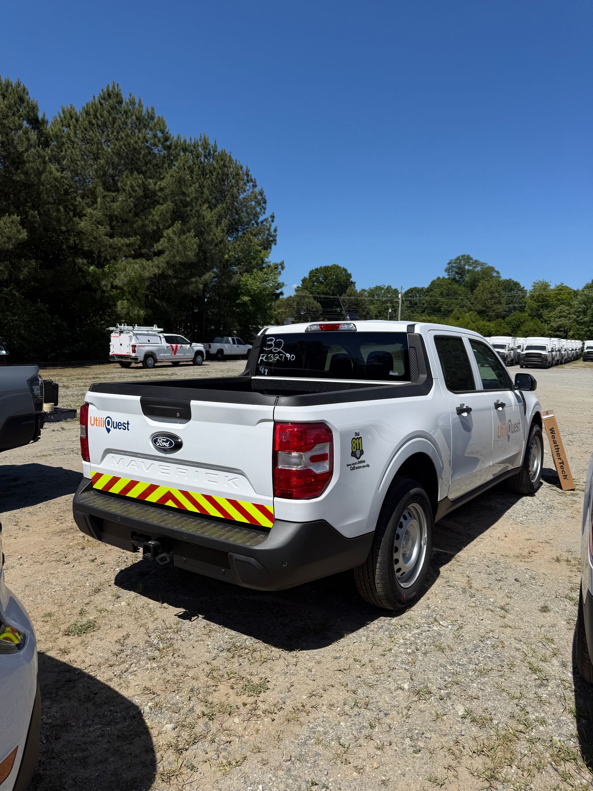 White pickup truck parked on gravel lot under trees, rear view with yellow chevron safety markings.