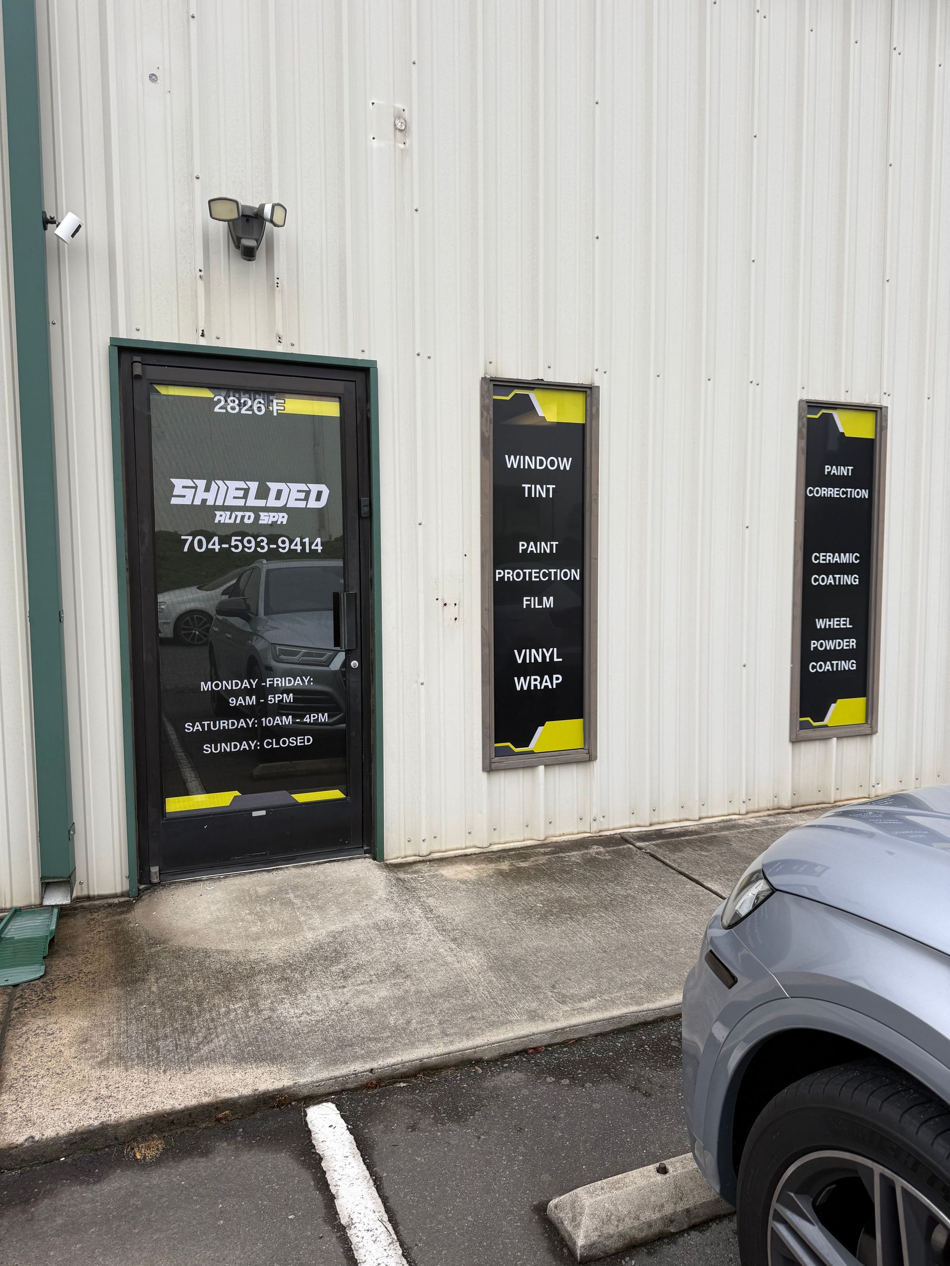 Exterior of a building with black-and-yellow signs beside a door and a parked car nearby