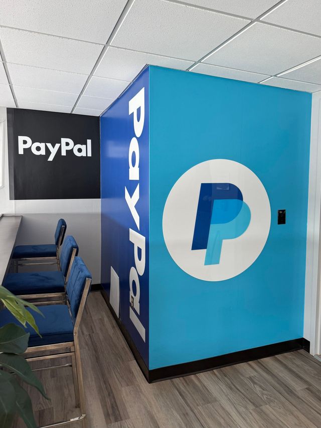 PayPal office corner with blue branded cubicle and chairs near a plant
