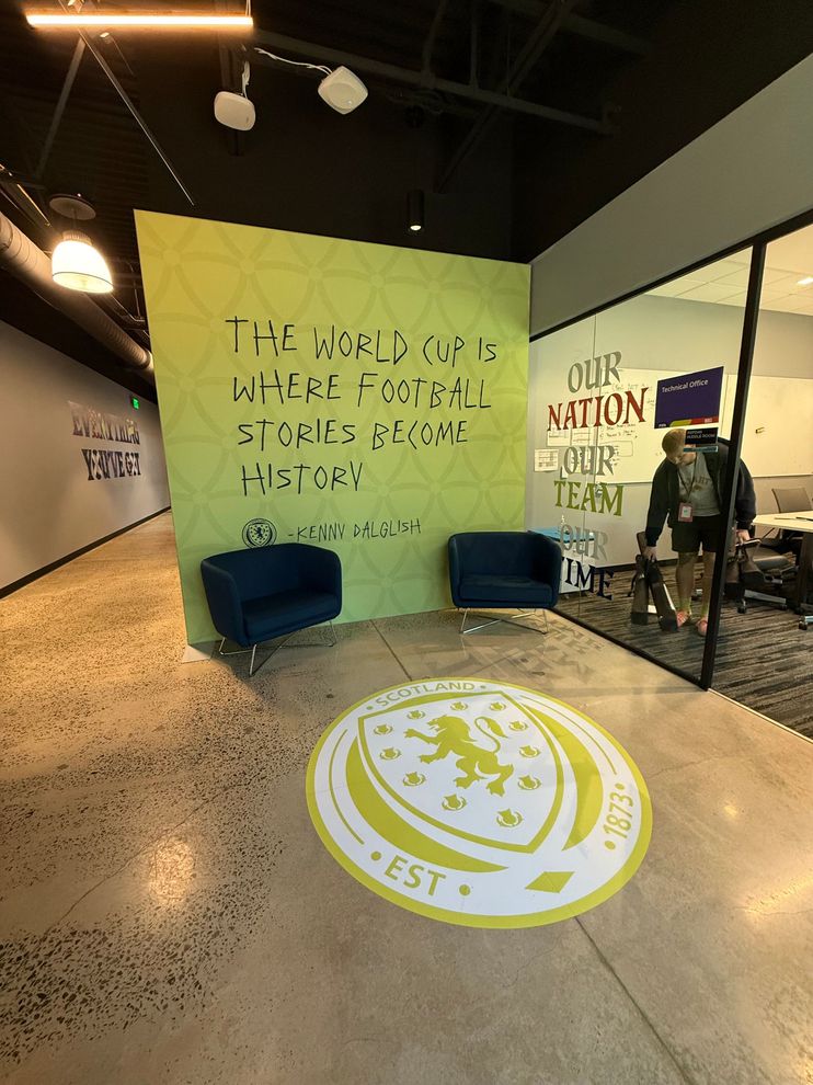 Lobby display with green mural, blue chairs, wall art, and a circular floor logo in a modern indoor space