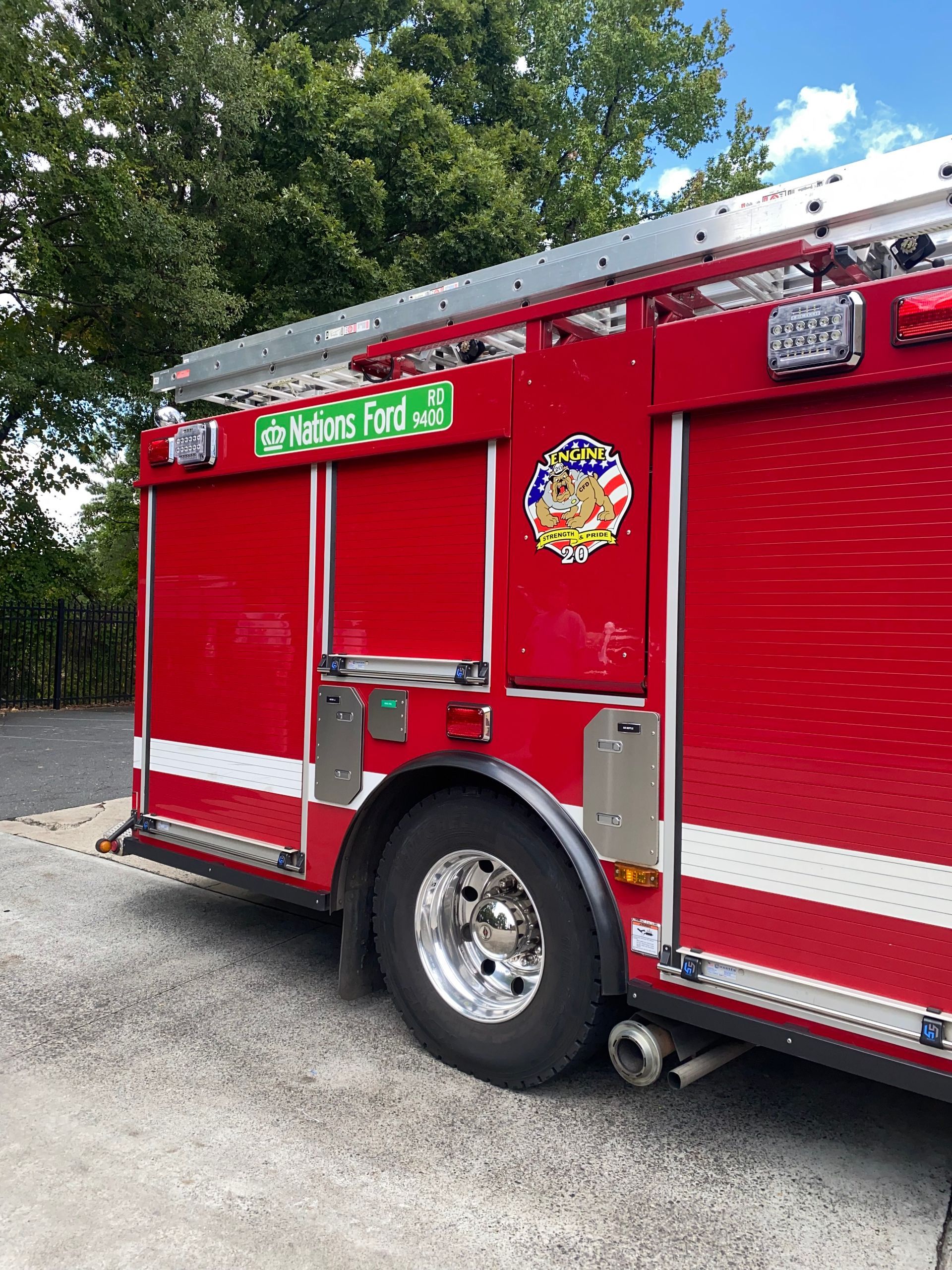 Red fire truck parked on gravel near trees, with green “STOWE NO. 2” sign and side compartment doors.