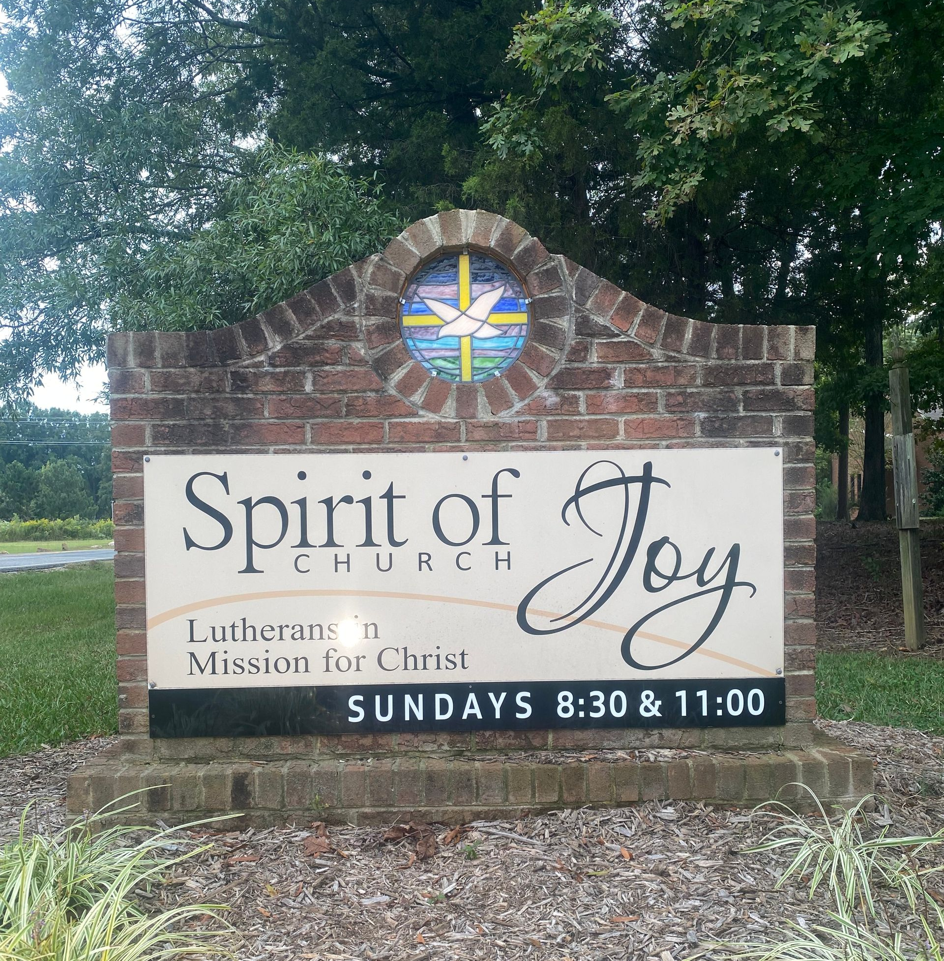 Church sign reading “Spirit of Joy Church” with Sunday service times beneath a brick archway.