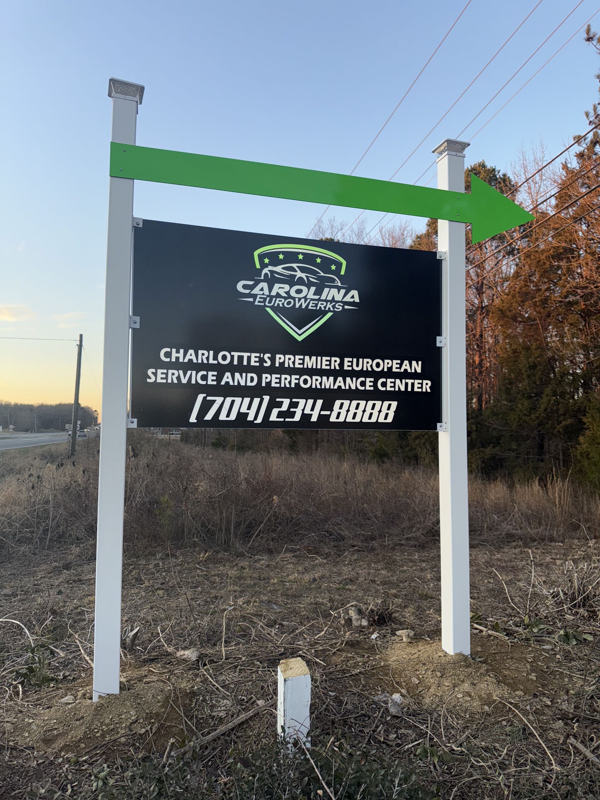Outdoor business sign for Charlotte’s Premier European Service and Performance Center, with a green top panel and black signboard.
