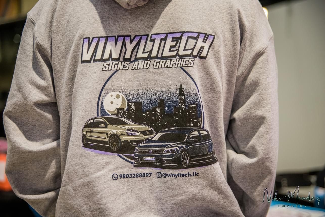 Person wearing a gray “VINYLTECH” sweatshirt with car graphic on the back.