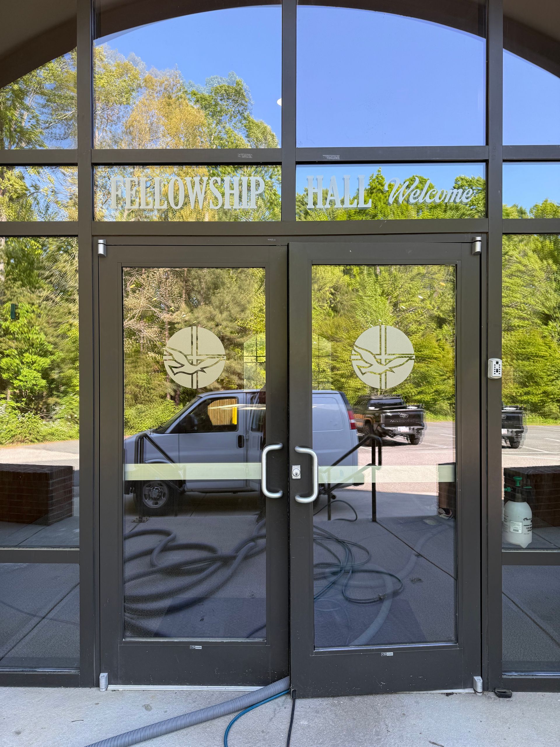 Glass storefront doors reflecting a parked white car and trees outside on a sunny day