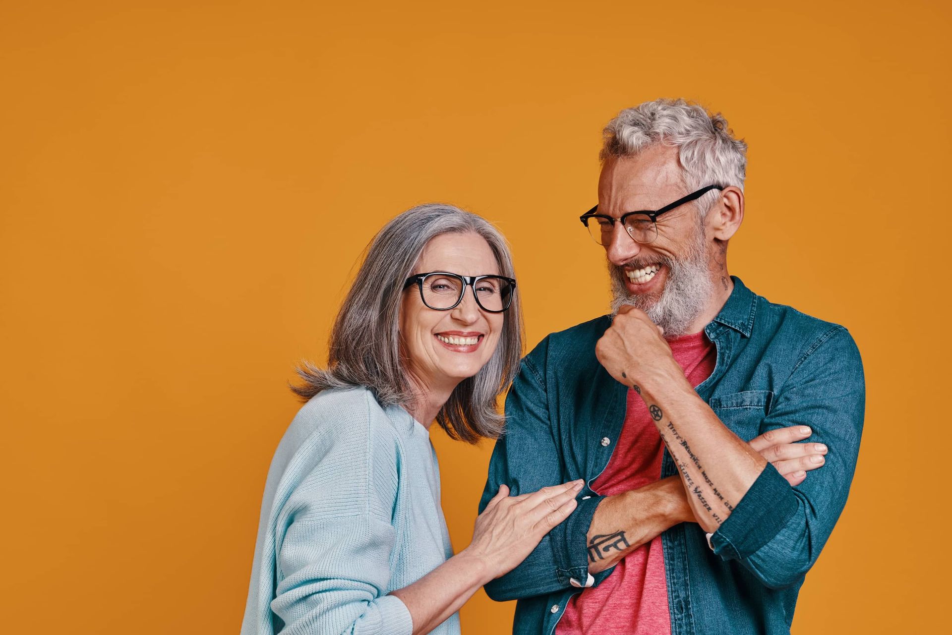 Older man kissing an older woman on the cheek; they are smiling on a beach.