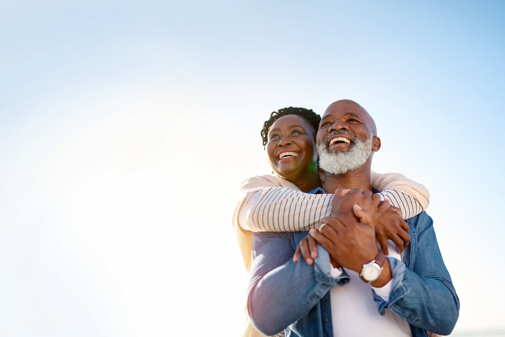 Older man kissing an older woman on the cheek; they are smiling on a beach.