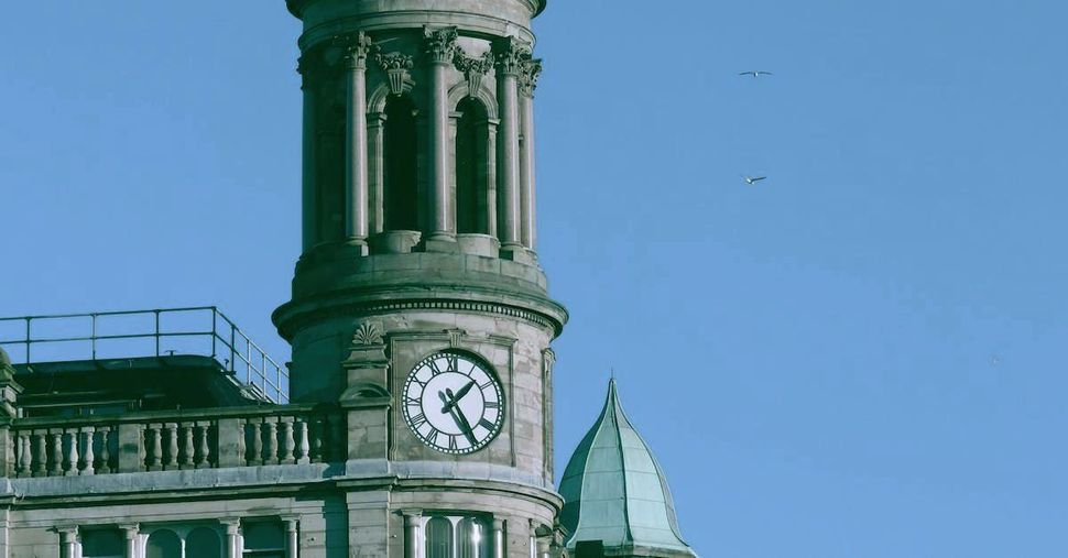 Clock tower on a building with ornate architecture against a bright blue sky.
