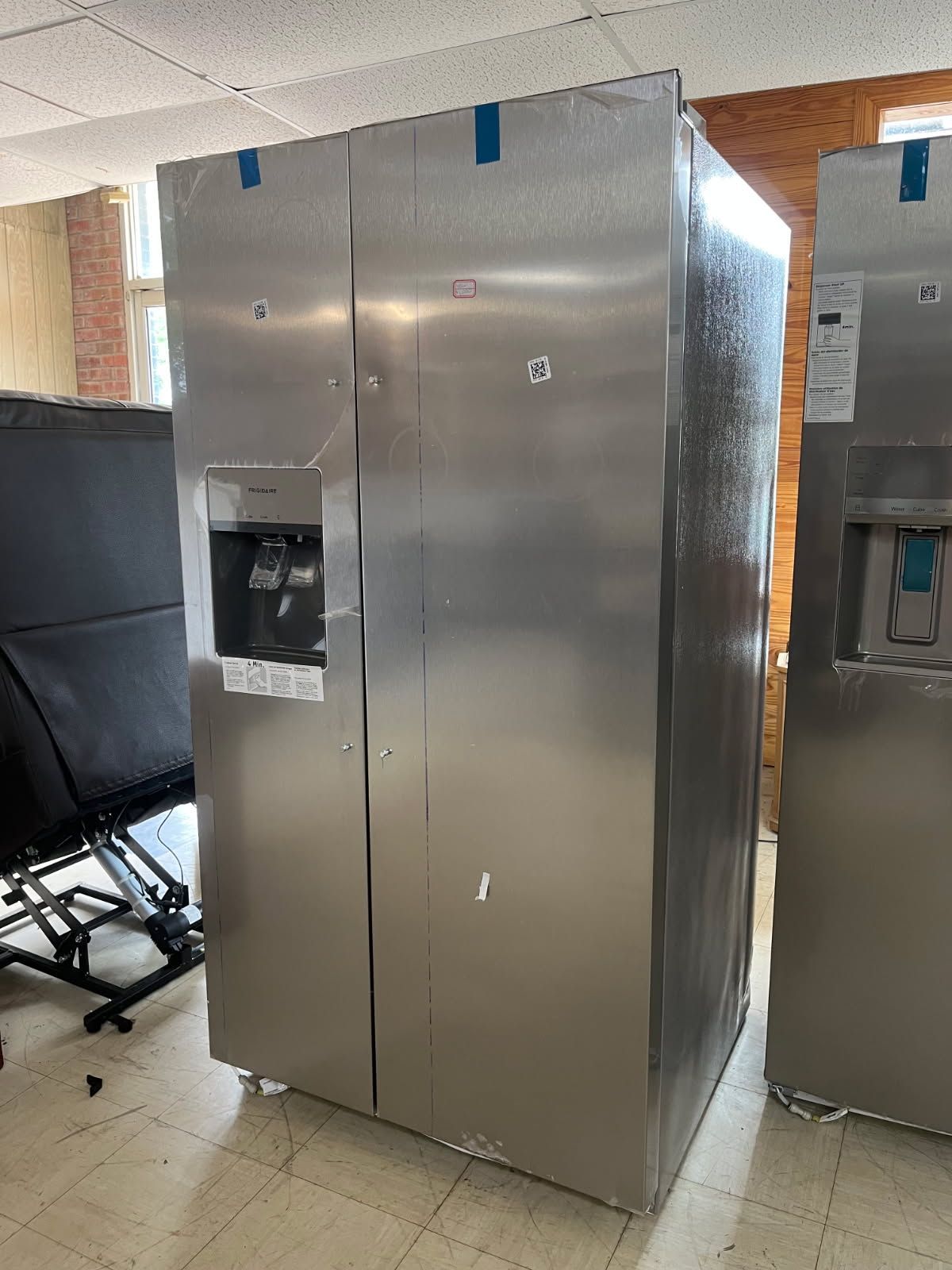 Stainless steel refrigerator in a showroom with a black chair nearby