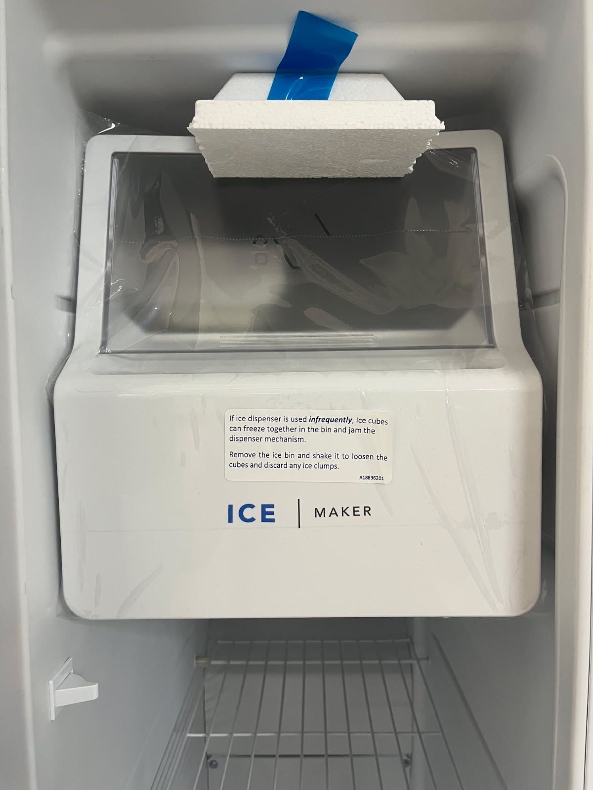 Ice machine with open bin and blue tape in a freezer compartment