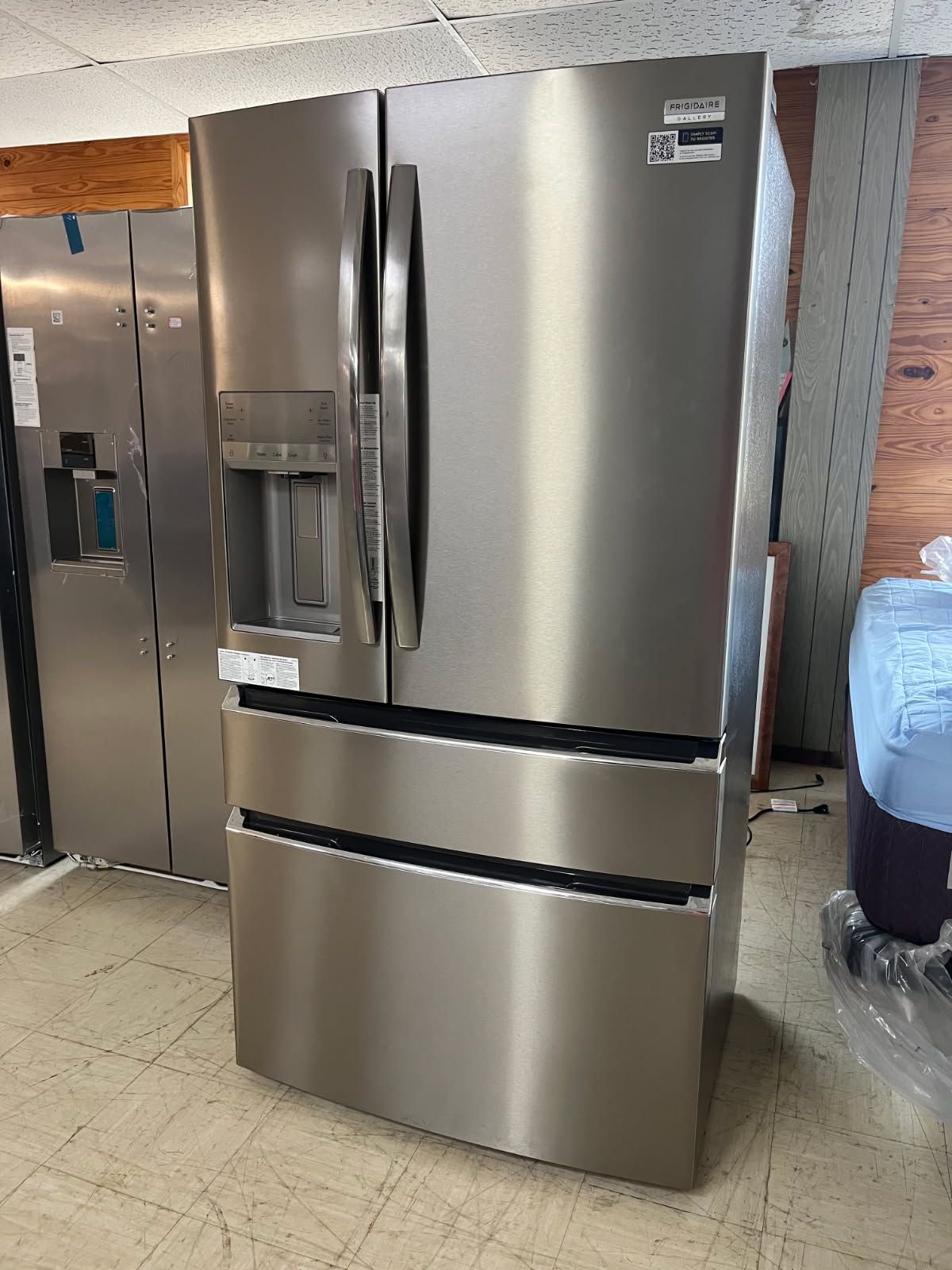 Stainless steel French-door refrigerator with bottom freezer drawer in an appliance showroom.