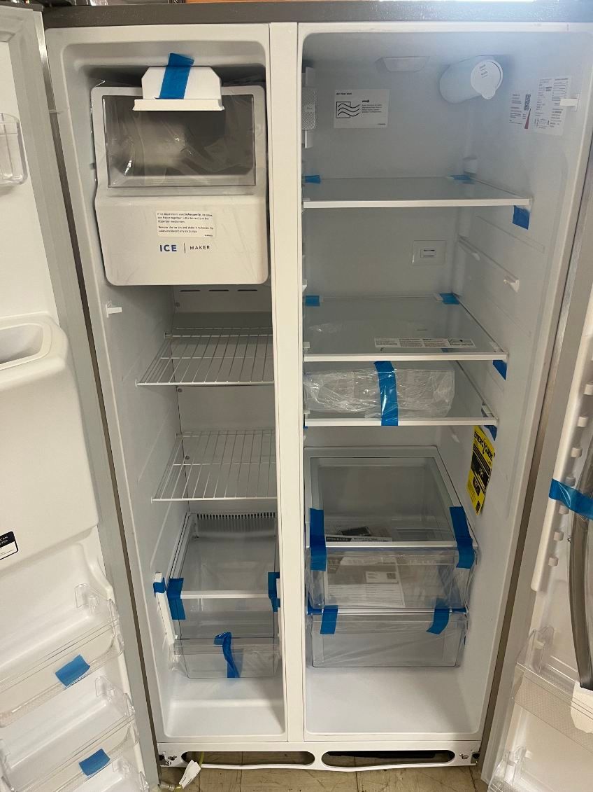 Open refrigerator with empty shelves, a water dispenser, and blue tape securing the doors and drawers.