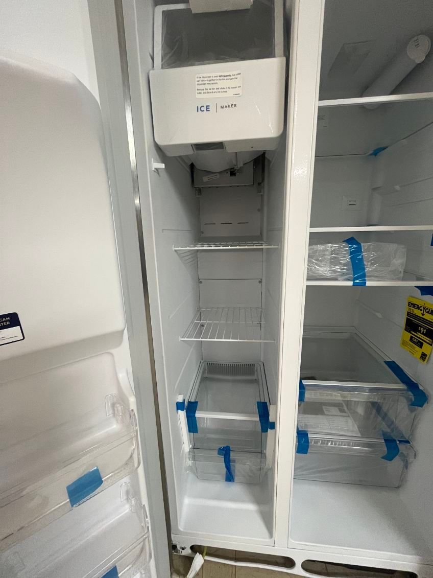 Open refrigerator with empty shelves, freezer section, and blue tape on the drawers.