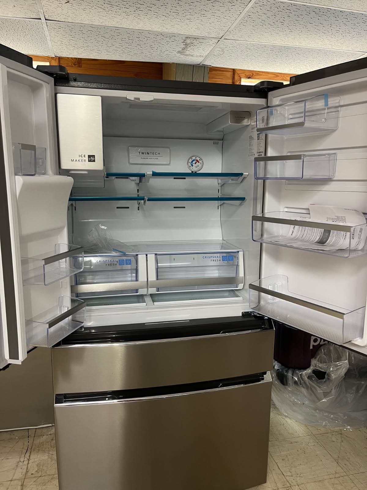 Open refrigerator with empty glass shelves and bottom freezer in a kitchen-like space