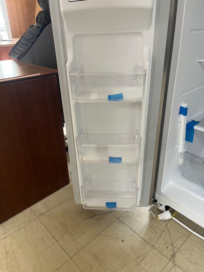 Open refrigerator door showing empty white shelves and clear drawers with blue handles