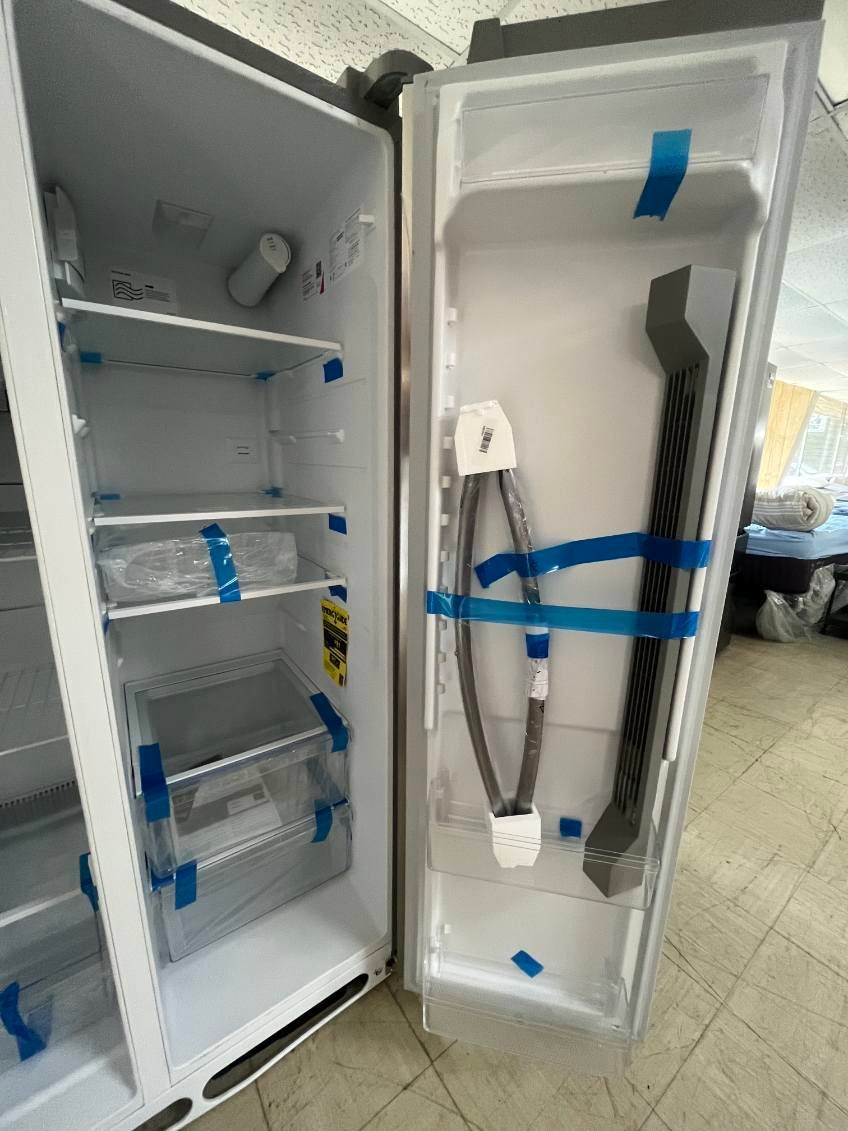 Open refrigerator with blue tape and shelves, beside a tall panel with attached cable in a workshop.