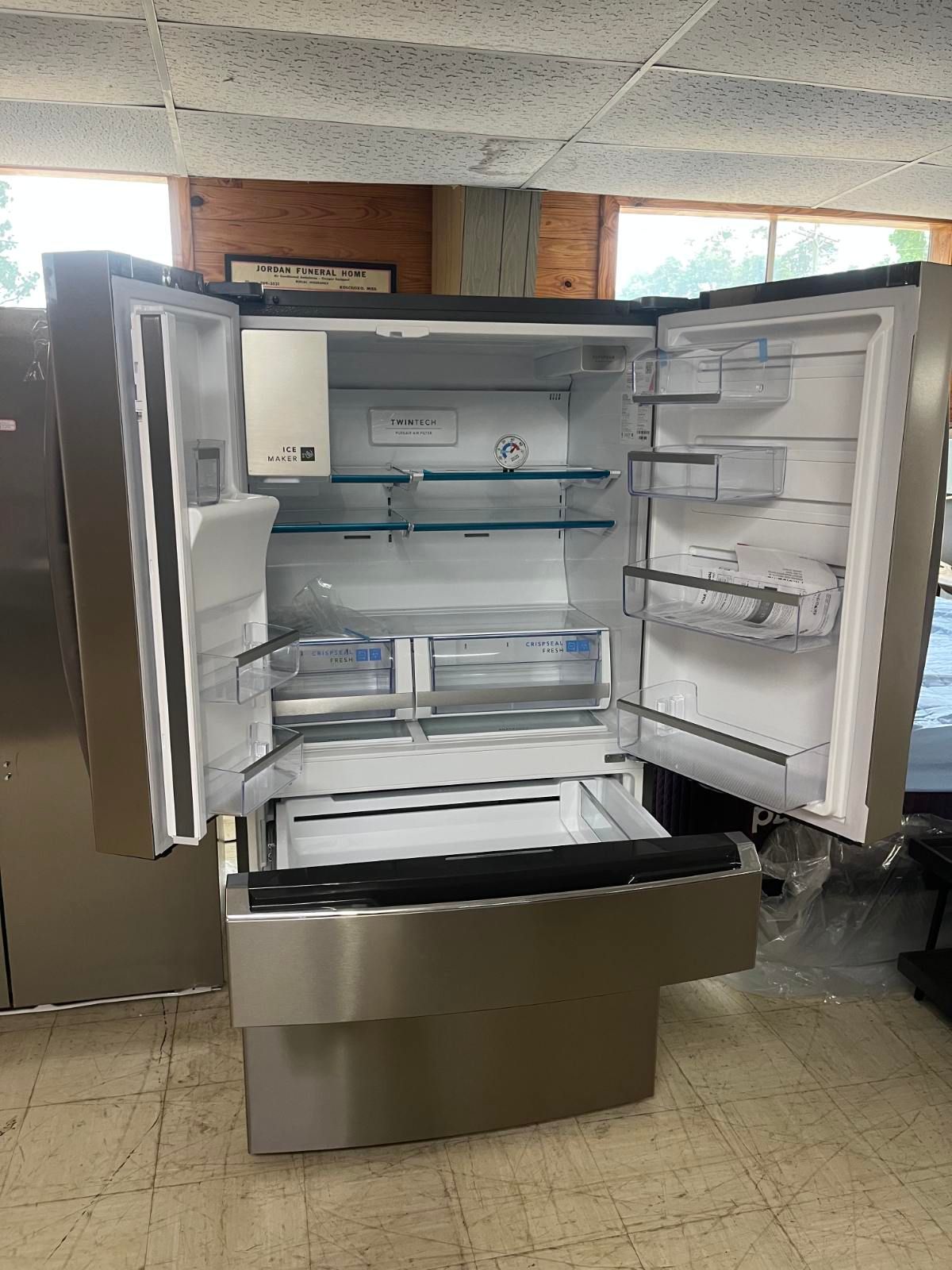Open stainless-steel refrigerator with glass shelves and drawers, in a kitchen or showroom.