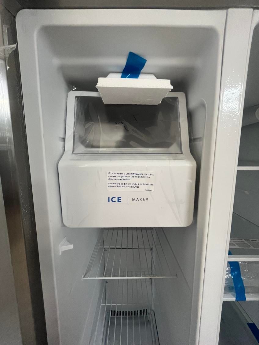 Ice maker inside a refrigerator with a white flap and blue tab.
