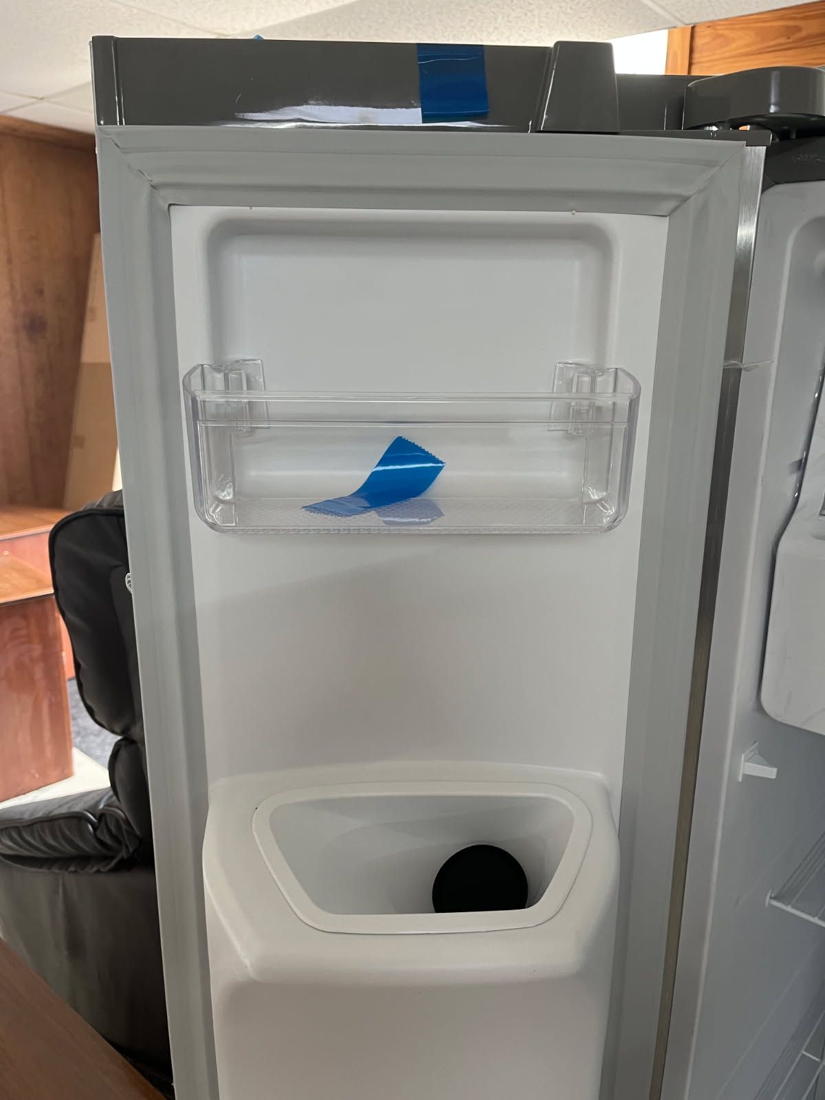 Open mini fridge with clear door shelf holding a blue tape tab, viewed from inside.