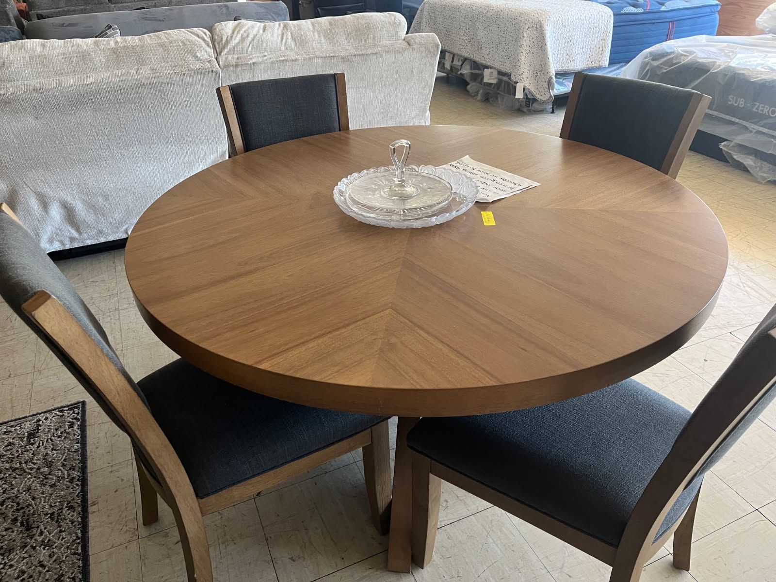 Round wooden dining table with four dark chairs and a decorative tray in a living room