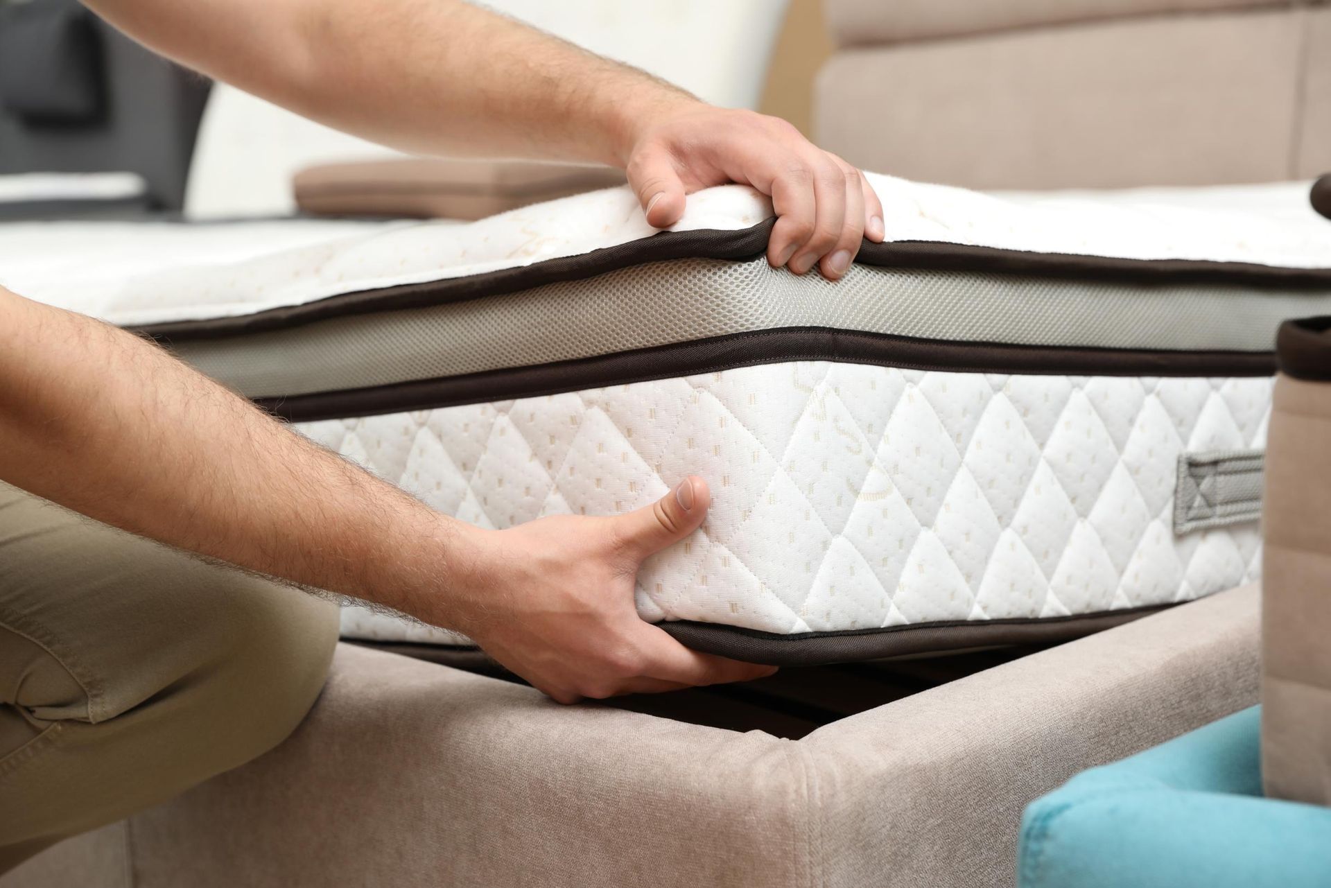 Hands lift a white quilted mattress from a beige sofa in a living room