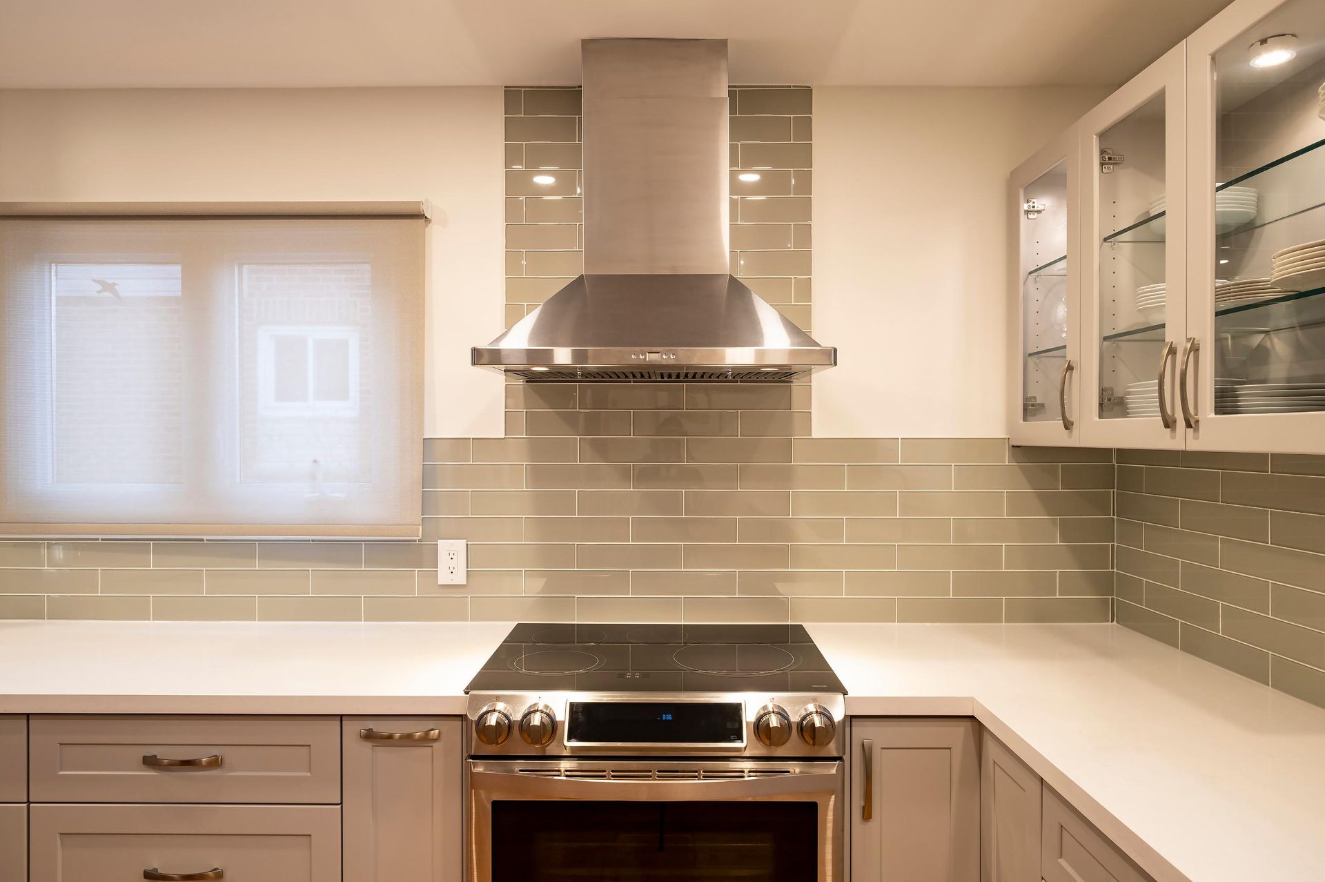 Modern kitchen with stainless steel range hood, beige tile backsplash, and white cabinets