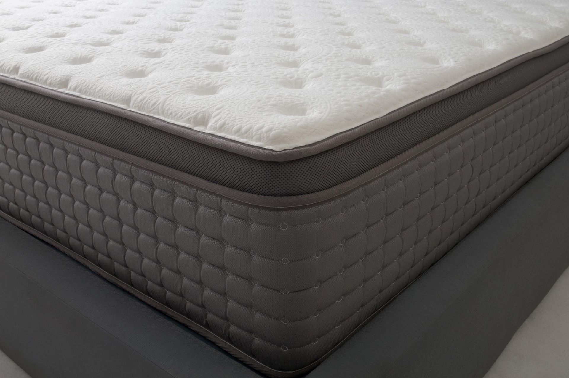 Close-up of a gray and white quilted mattress corner on a bed frame