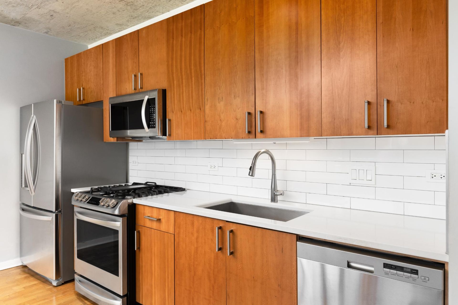 Modern kitchen with wood cabinets, stainless steel appliances, white backsplash, and light countertops