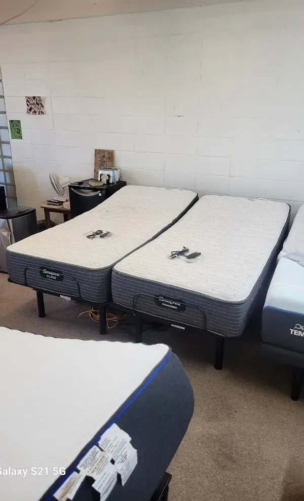Hospital room with two adjustable beds and white mattresses, viewed from the foot of the beds.
