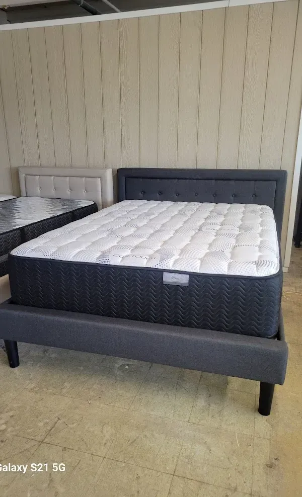 Two gray upholstered beds with white mattresses in a showroom against a beige paneled wall.