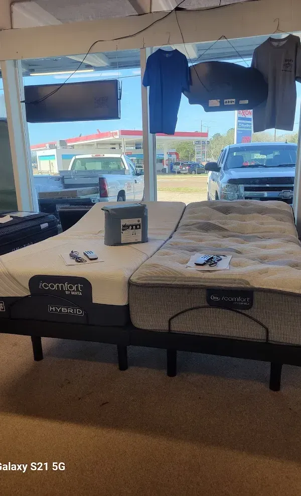 Mattress display inside a store, with blue shirts and parked cars visible through the front windows.