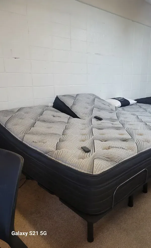 Black bed with wrinkled white bedding against a white wall in a bare bedroom