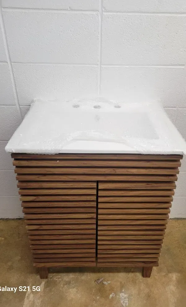 Wooden cabinet with horizontal slats and a white sink countertop against a tiled wall.