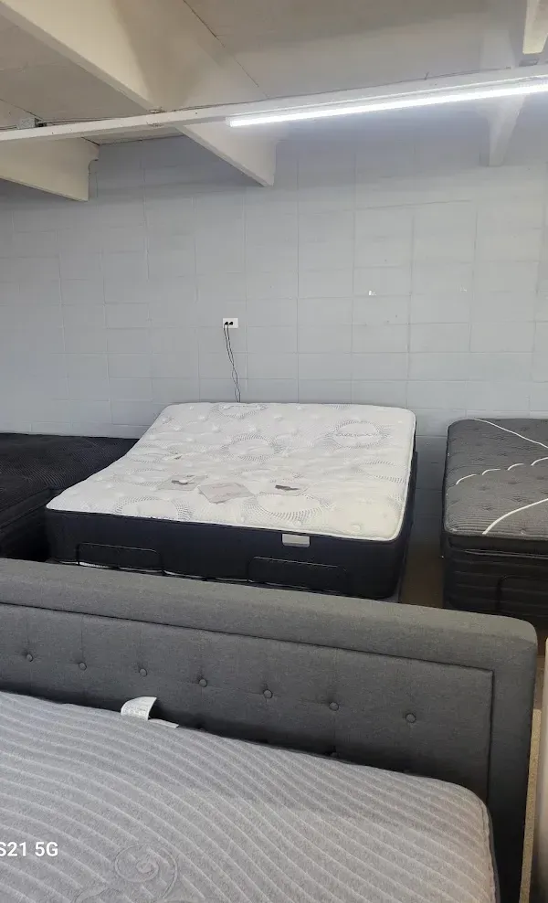 Mattresses displayed in a showroom, including gray and white beds against a tiled wall