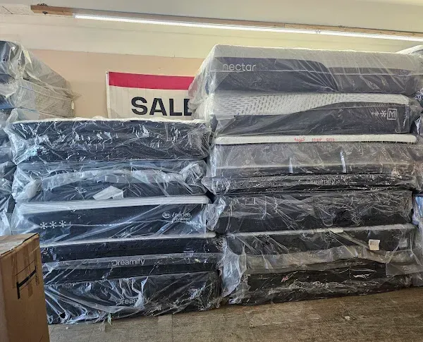Stacks of plastic-wrapped black mattresses in a store, with a SALE sign in the background.