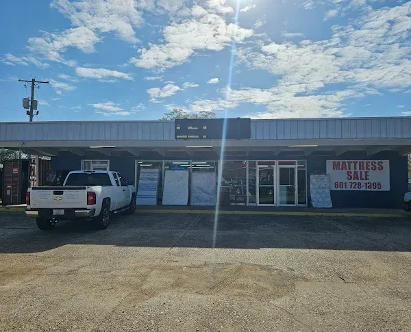 Mattress store storefront with a white pickup truck parked outside under a blue sky.