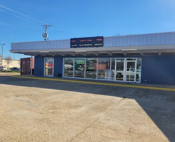 Small storefront with glass doors and windows under a blue sky, viewed from the parking lot