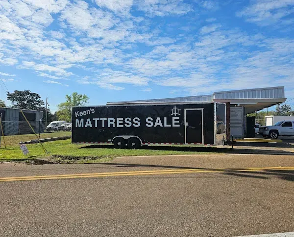 Mattress sale sign on a trailer beside a roadside building under a blue sky