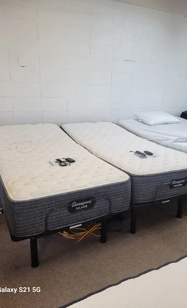 Two hospital-style beds with white mattresses in a plain room, one with a pillow.
