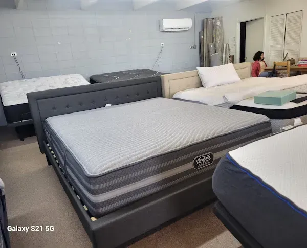 Mattresses and beds displayed in a showroom with white tiled walls and mirrors.