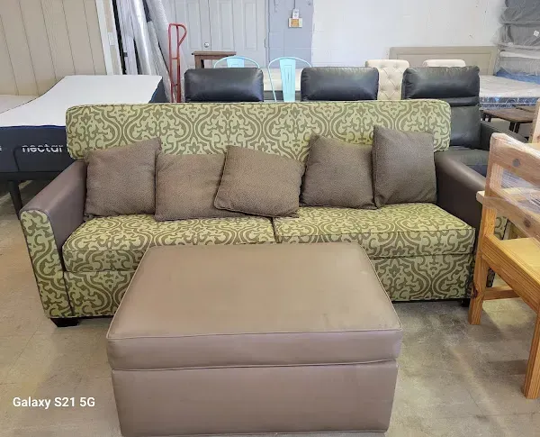 Green patterned sofa with brown cushions and a beige ottoman in a furniture showroom