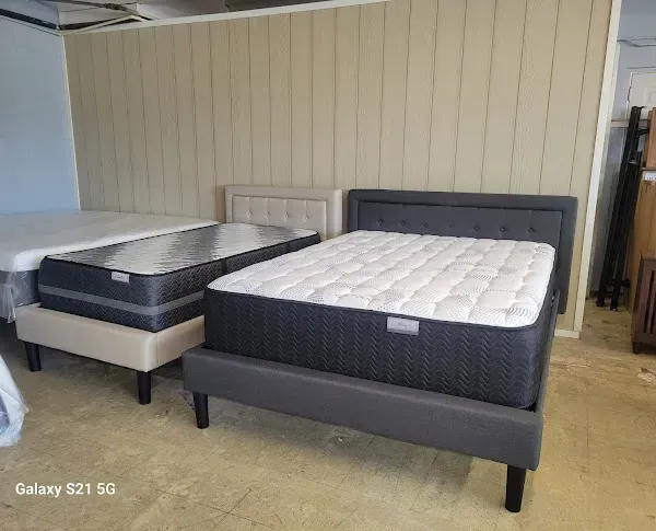 Two dark gray upholstered beds with white mattresses in a showroom area.