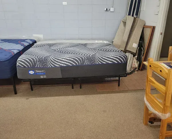 Bedroom with two beds, a gray patterned mattress, and stacked boards leaning against a wall.