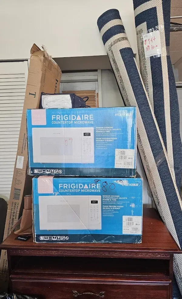 Two stacked Frigidaire window air conditioner boxes on a wooden dresser, with rolled rugs beside them.