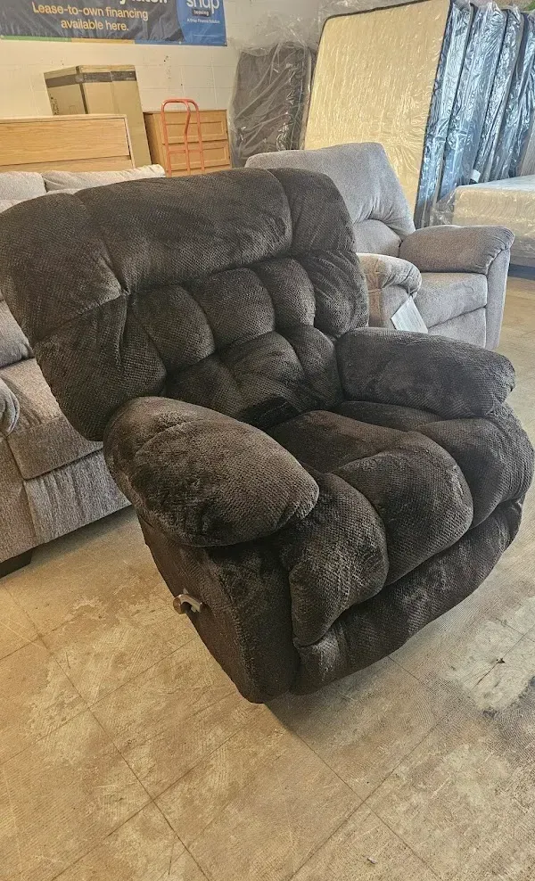 Dark brown plush recliner chair in a storage or workshop space with boxes and furniture in the background