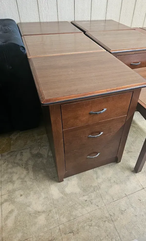 Wooden desk with three drawers and a brown laminate top in a room with tiled floor.