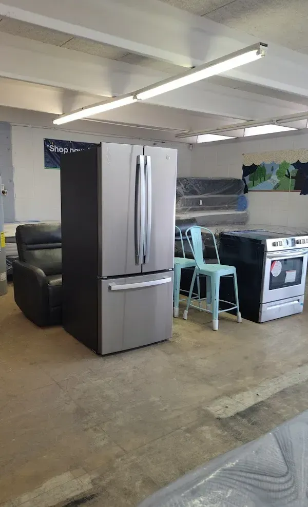 Basement storage area with a stainless steel refrigerator, desk chair, stove, and sofa under fluorescent lights